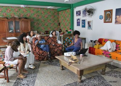 Um grupo de sete pessoas se reuniu na sala de estar; algumas estavam sentadas nos móveis e outras no sofá, com um laptop e um projetor sobre a mesinha de centro.