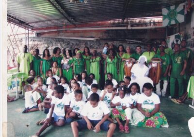 Um grande grupo de pessoas vestidas com roupas verdes e brancas se reuniu para um evento comunitário, com as crianças sentadas na frente e os adultos em pé atrás delas.