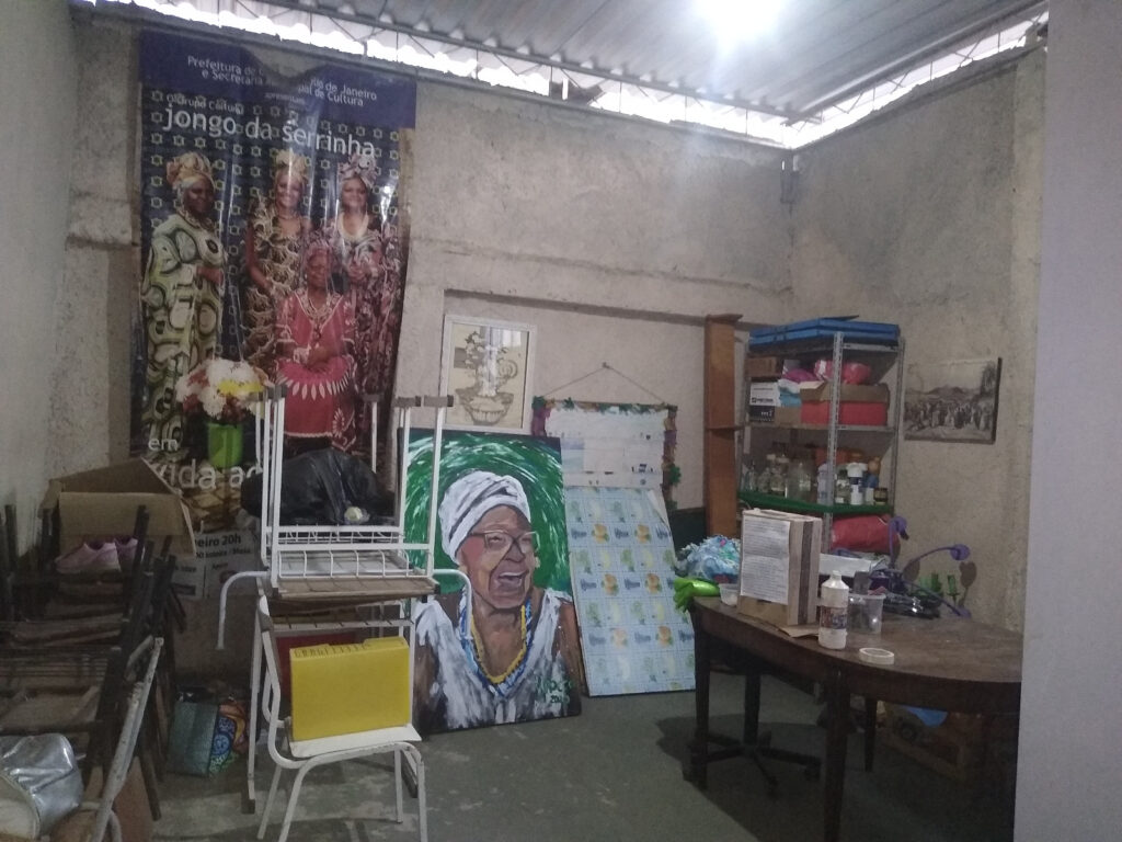 Um espaço interno com um grande pôster mostrando pessoas em trajes tradicionais e um retrato de uma senhora idosa usando um lenço na cabeça.