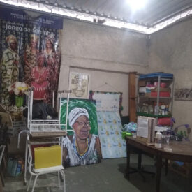 Um espaço interno com um grande pôster mostrando pessoas em trajes tradicionais e um retrato de uma senhora idosa usando um lenço na cabeça.